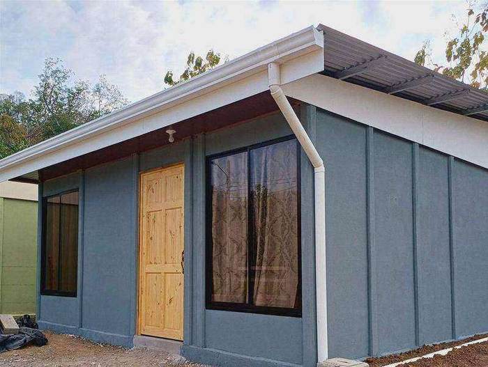 Casa gris azulada de una planta con puerta de madera y ventanales, entregada en Nicoya, Guanacaste
